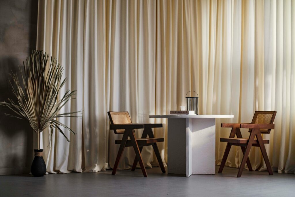 Elegant Japandi-style interior featuring wood armchairs, white table, and neutral curtains.