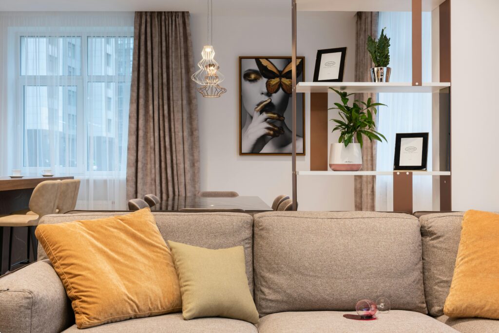 Light room interior with soft couch with pillows and glass of spilled wine near shelves and counter with chairs near window with curtains, Colori casa