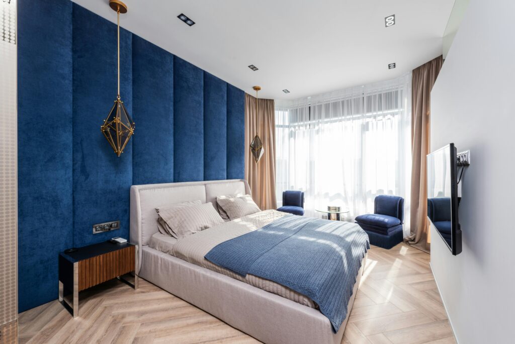 Elegant bedroom with blue accent wall, stylish furniture, and ample natural light.