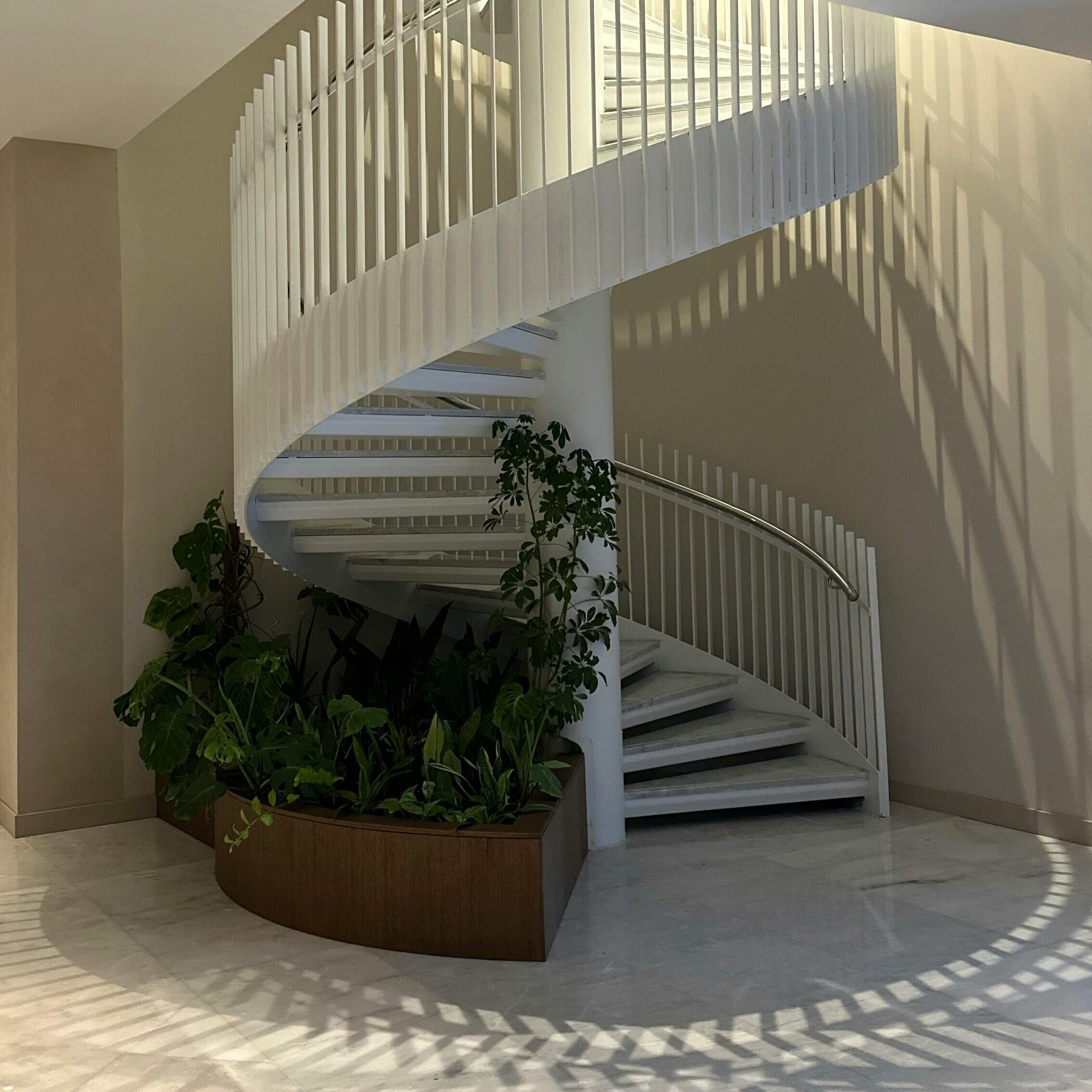 A stunning indoor spiral staircase with plants in a modern architectural setting, offering elegance and style.