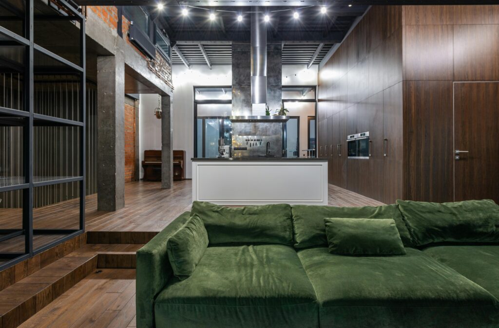 Spacious modern loft featuring an elegant green sofa, industrial decor, and sleek kitchen.