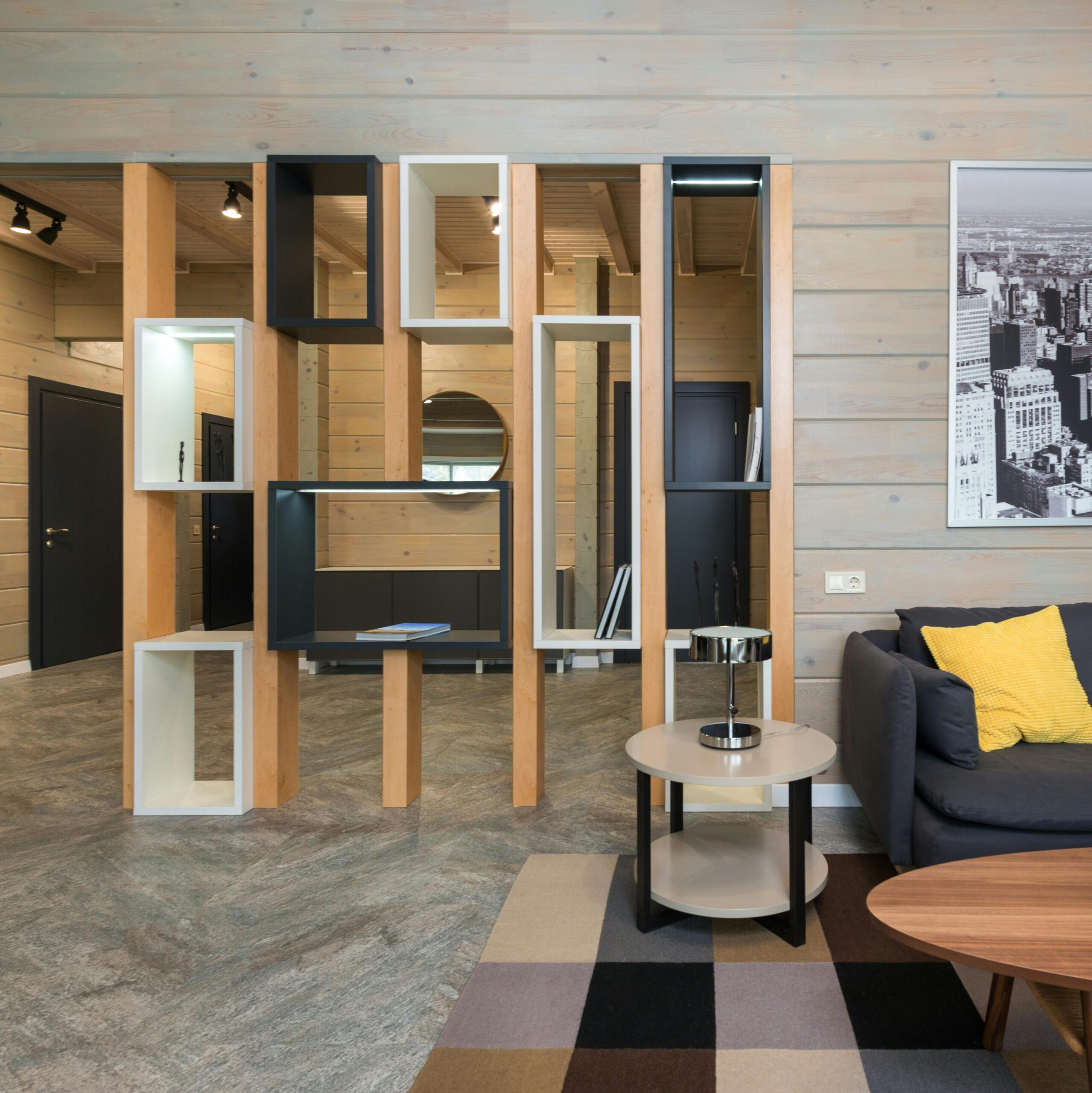 Modern apartment with sofa placed near round table with stylish geometric shelves separating living room from corridor