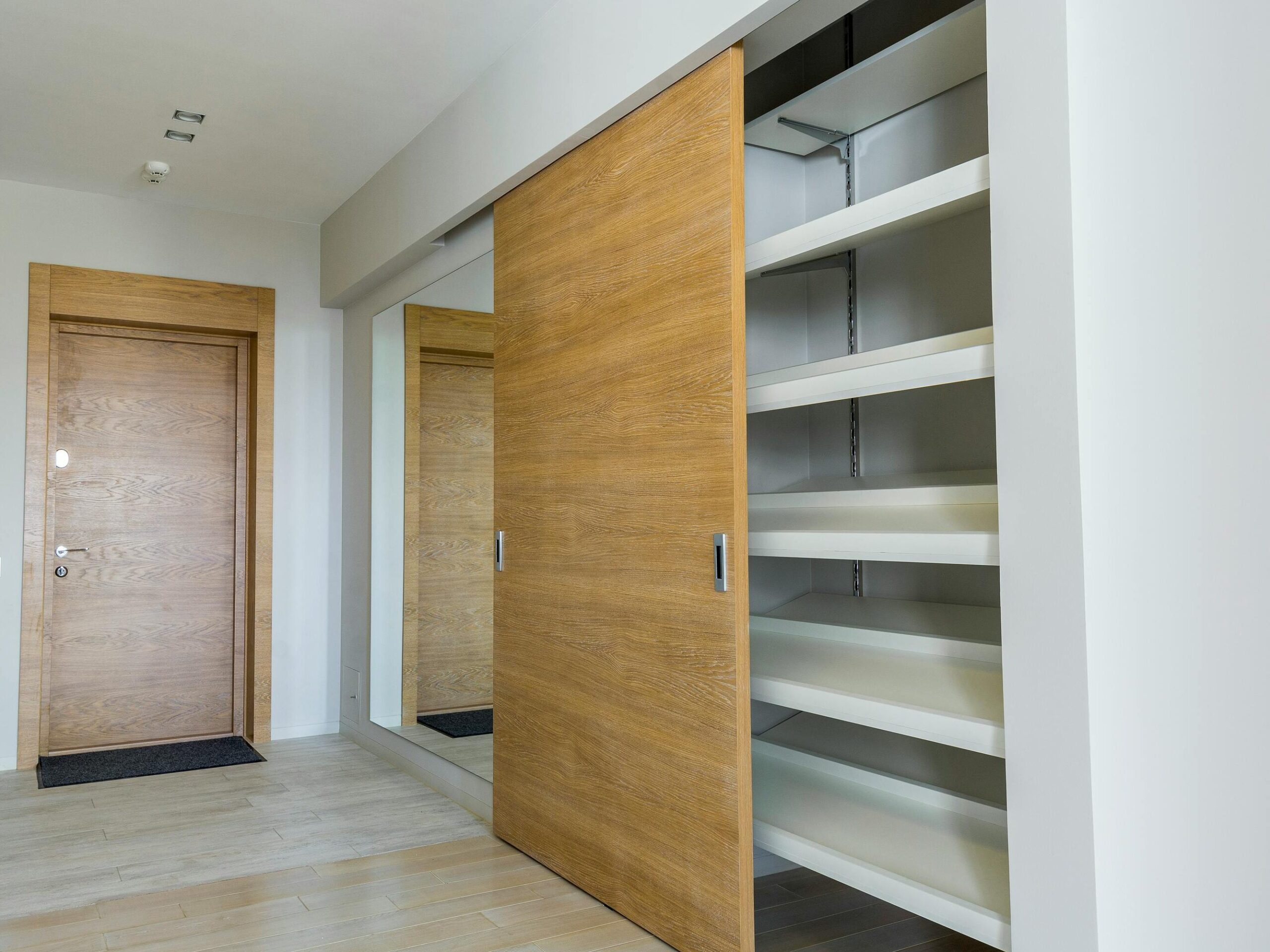 Elegant modern walk-in closet with wooden sliding door and empty shelves in a sleek minimalist style.