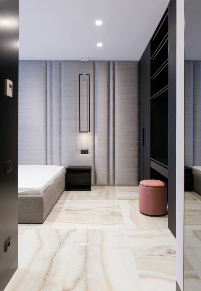Interior of contemporary house with mattress on bed near table and pouf near cabinet with shelves
