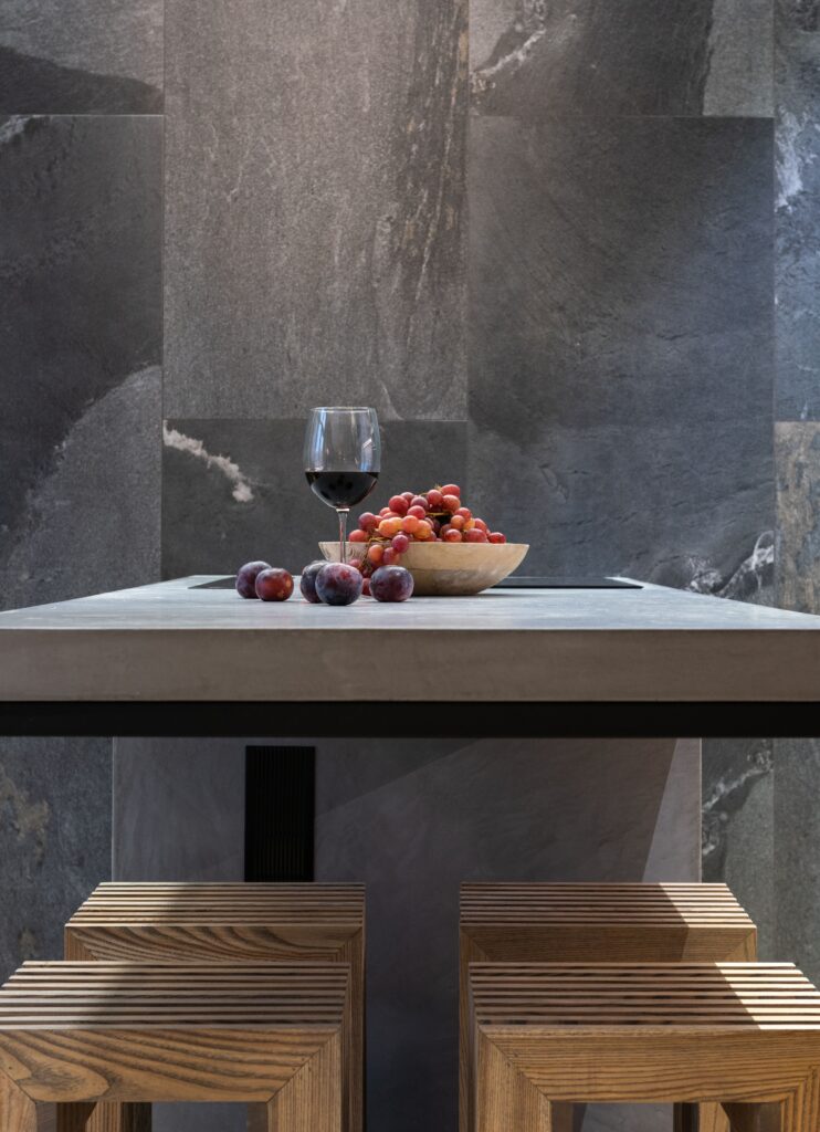 Modern dining table with a glass of red wine and a bowl of fresh fruits, featuring wooden stools. Cucina di lusso
