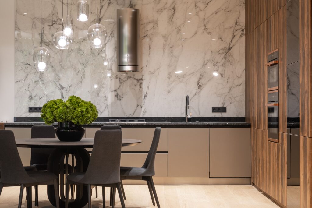 Comfortable chairs and round table with vase of fresh flowers in modern kitchen with wooden furniture and marble wall decorated with creative lamps, Cucina di lusso