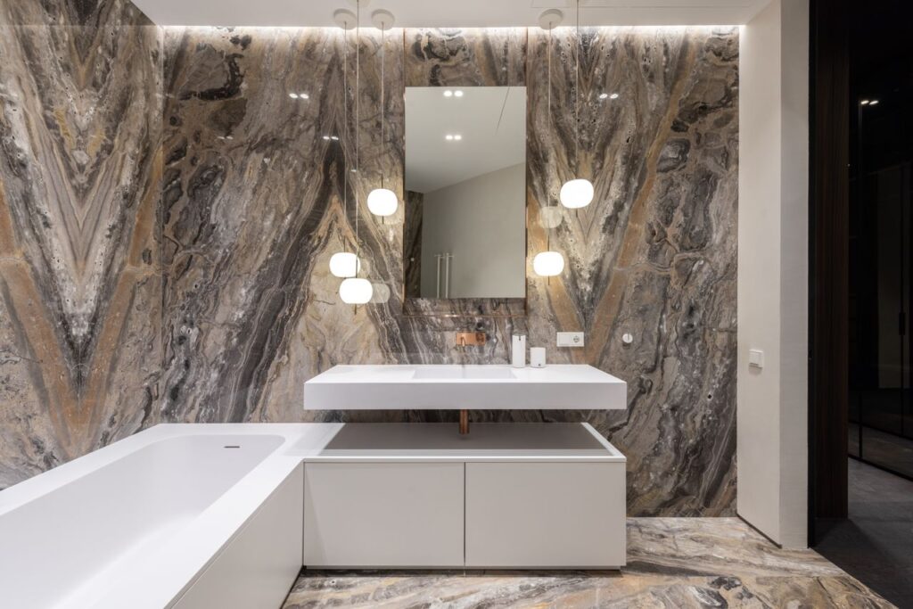 Interior design of modern bathroom with mirror hanging on wall above sink and big bathroom and illuminated with round lamps