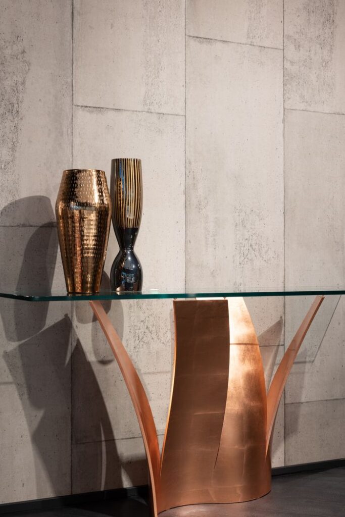 Elegant vases placed on creative table with glass top near gray wall in modern apartment