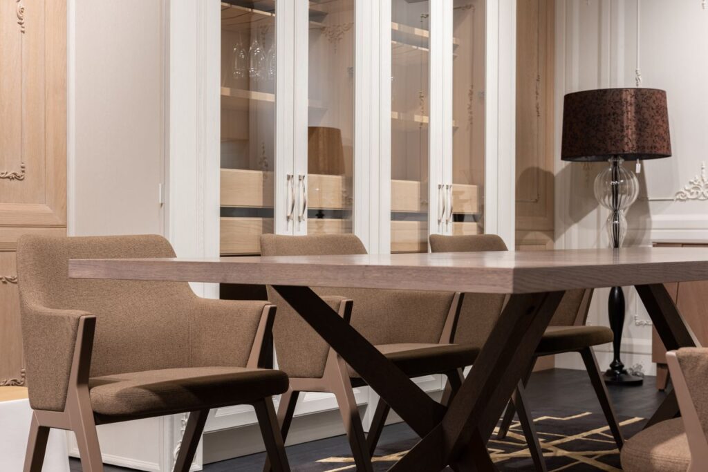 Long table with set of brown chairs placed near white cupboards in dining room with tall lamp in stylish apartment, Arredamento contemporaneo