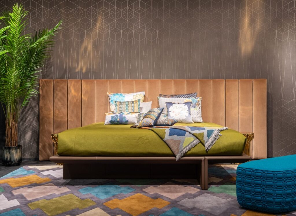 Comfortable bed with headrest and cushions placed on coverlet in bedroom with bright carpet and settee, Arredamento contemporaneo