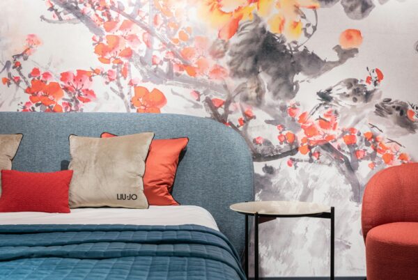 Comfortable bed with colorful cushions and blanket placed at painted colorful wall near side table and armchair in modern apartment
