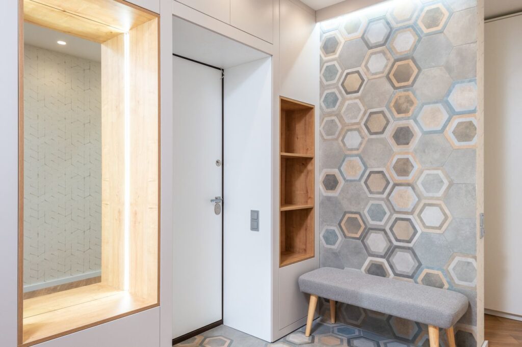 Lobby interior with entrance door and wall with hexagonal ornament against fabric bench and mirror with shiny light at home, Cappottiera da ingresso