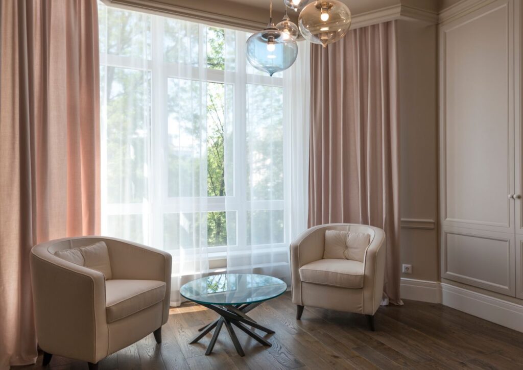 Interior of stylish room with soft armchairs and glass round table near huge window