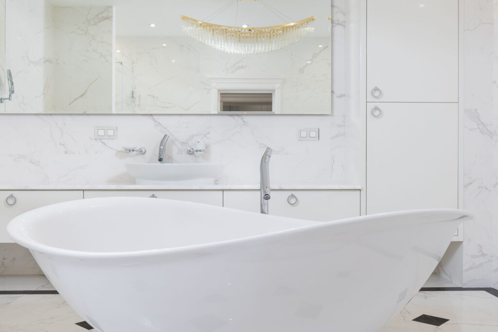 Interior of marble white modern bathroom with mirror reflecting shimmering huge chandelier in apartment. Bagno di lusso.