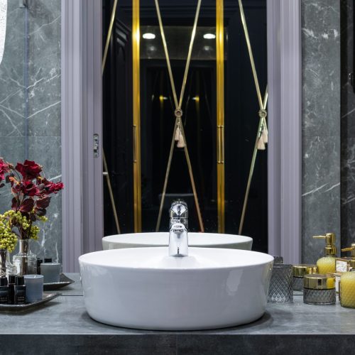 Washstand with tap between flower in vase and assorted hygiene products reflecting in mirror at home, bagno di lusso.