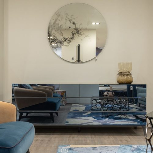 Modern interior of luxury living room with comfortable armchair and shining table against mirror on wall and glowing dresser